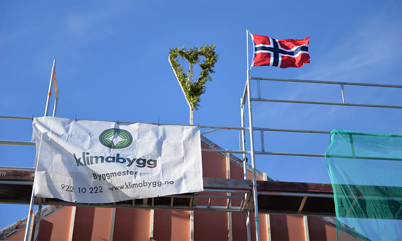 Stillastillas med Klimabygg-banner, grønt ceremonihjerte og norsk flagg mot blå himmel.