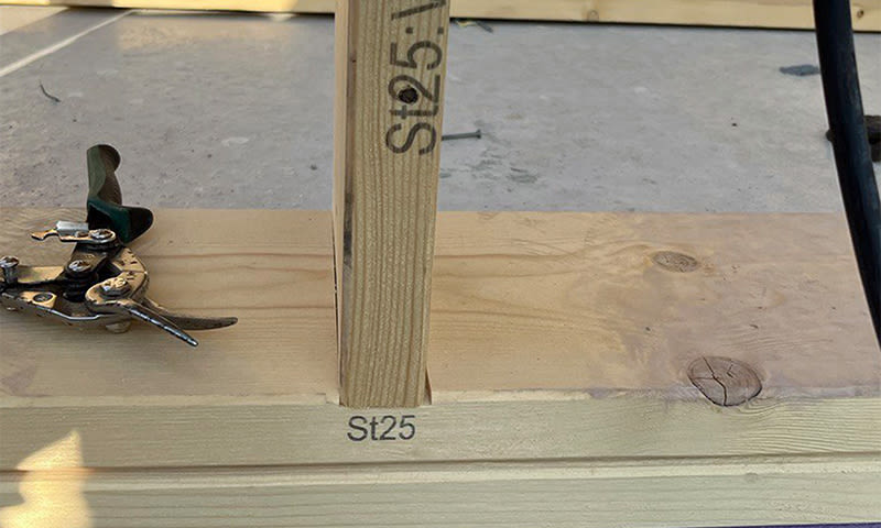 Lyse trebjelker merket "St25" i T-kryss med sort/grønn håndsaks på byggeplass.