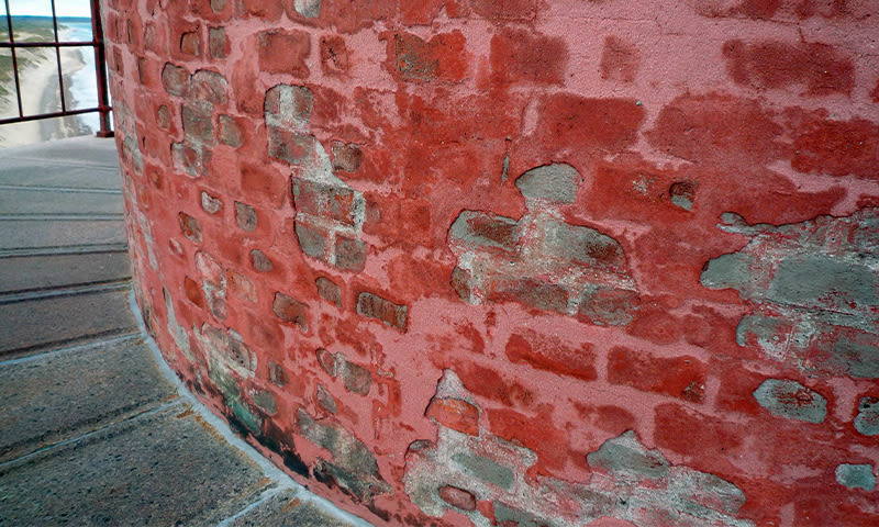 Buet rødmalt mur med slitt overflate, grå flekker, betonggulv og rekkverk mot hav