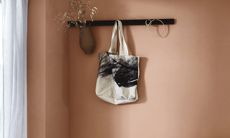 Minimalistisk interiør: terrakottavegg med svart stang, tørkede blomster, metallringer og tøypose