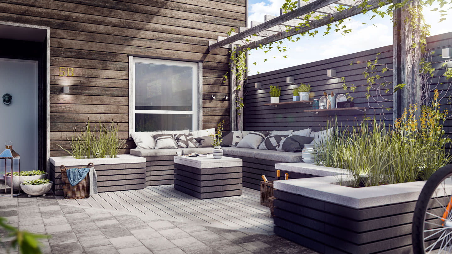 Solrik uteplass med mørkt treverk, grå benk- og plantekasser, puter, grønne planter og pergola.