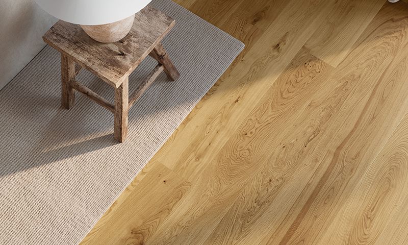 Rustikt brunt trebord med hvit lampe på beige teppe ved lyst eikegulv i sollys.