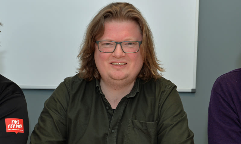 Ung mann med langt blondt hår og grønn skjorte foran hvit tavle i grått møterom.