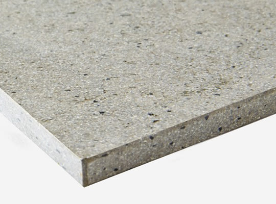 Nærbilde av skråstilt lys beige kvartsplate med små mørkgrå og svarte flekker.