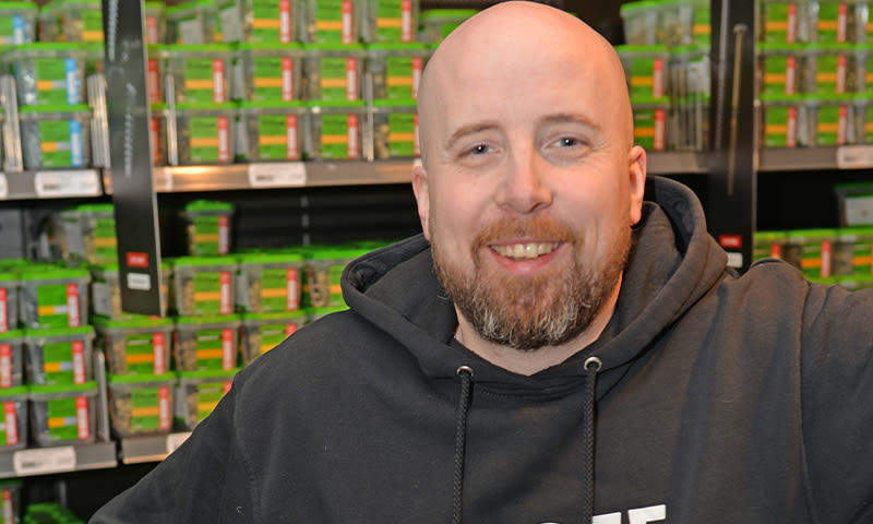 Mann i mørk hettegenser foran butikkhyller fylt med grønne esker.