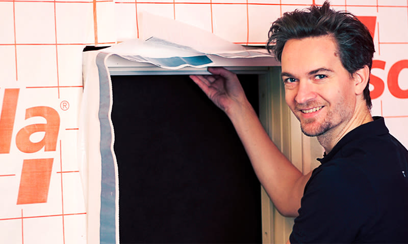 Håndverker fester hvit isolasjonsduk med rød tekst rundt vindusåpning