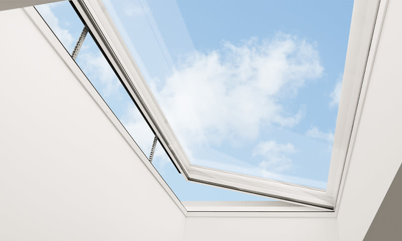 Åpen takluke med hvit ramme mot klar blå himmel med lette skyer