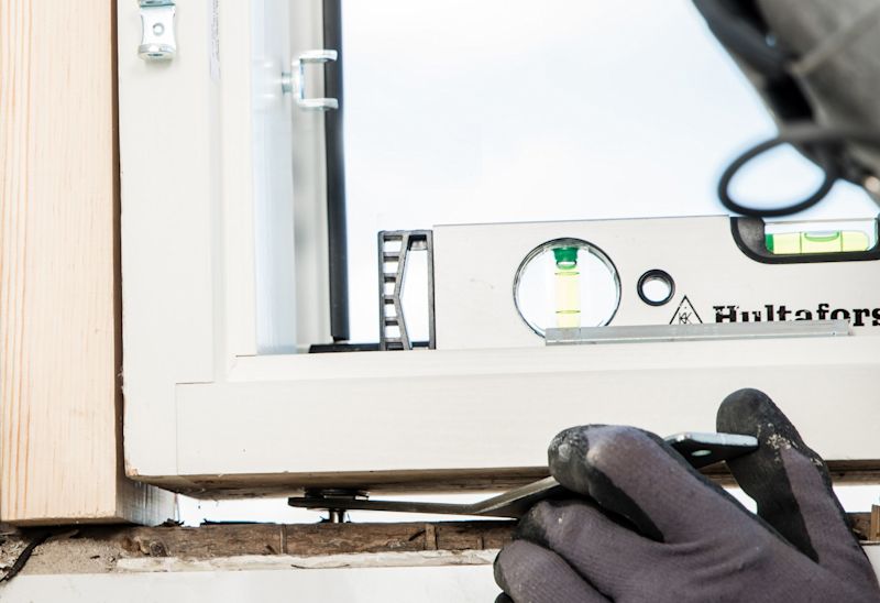 Hanskekledd hånd justerer hvit vinduskarm med grønn vater