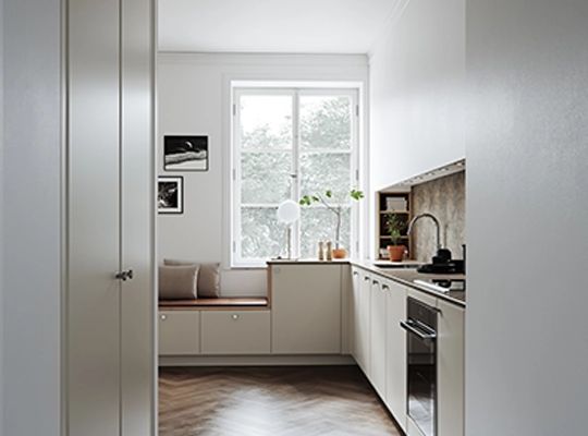 Moderne hvitt kjøkken med kjøkkenøy, mørk benkeplate, svart kran og høye skap med svarte håndtak.
