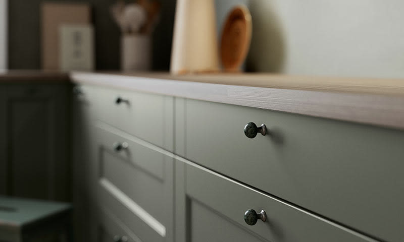 Nærbilde av lysegrønne kjøkkenskuffer med mørke grønne knotter og lys treplate.