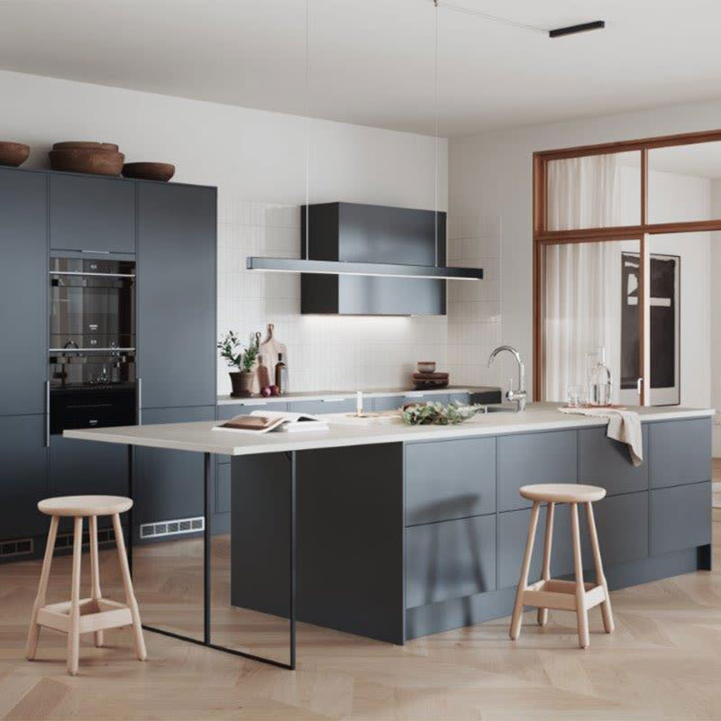 Moderne kjøkken med grå skap, lys benkeplate, kjøkkenøy, to lyse treskamler og vindu.