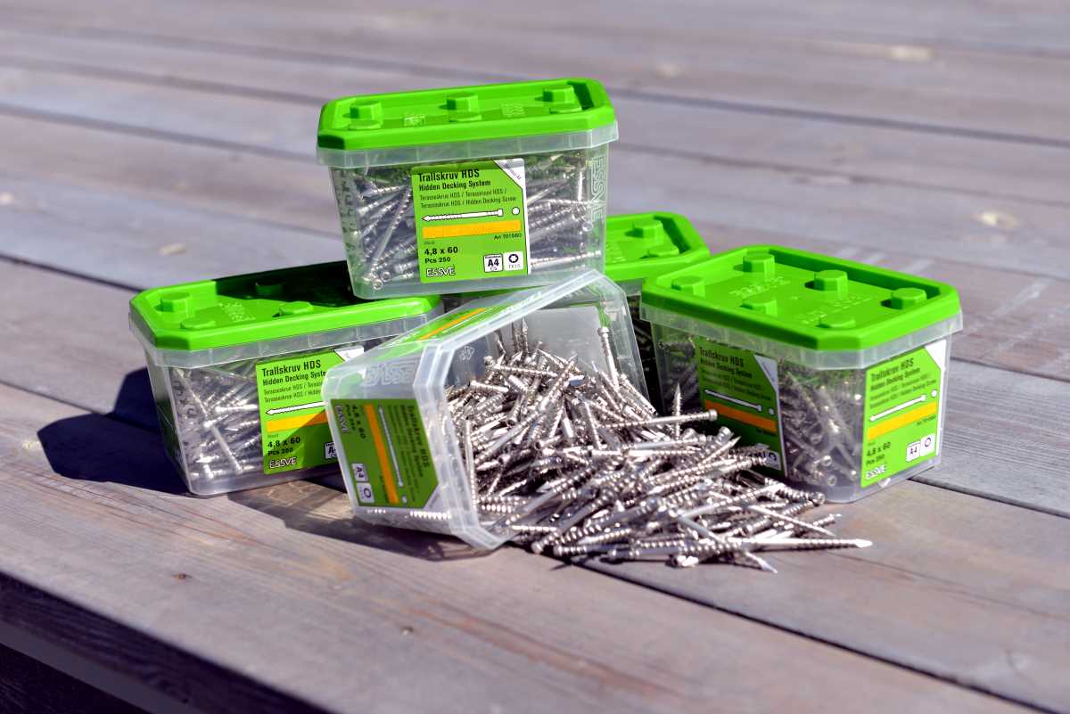 Grønne plastbokser med skruer på terrassebord, en boks veltet med sølvskinnende skruer