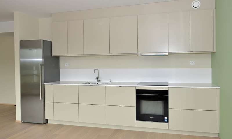 Moderne lys kjøkkeninnredning med beige skap, stålfrigo, innebygd ovn og vask