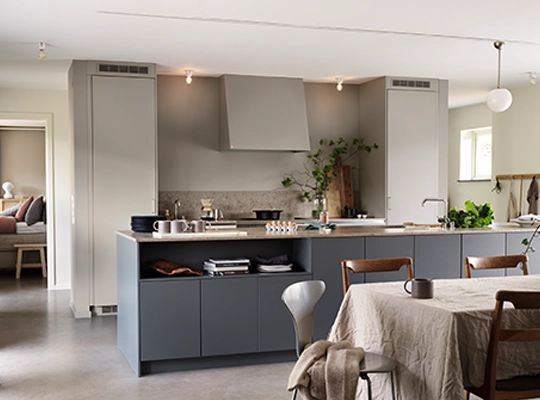 Moderne åpent kjøkken med grå skap, kjøkkenøy, spisebord med stoler og grønne planter. Lyst og minimalistisk interiør.