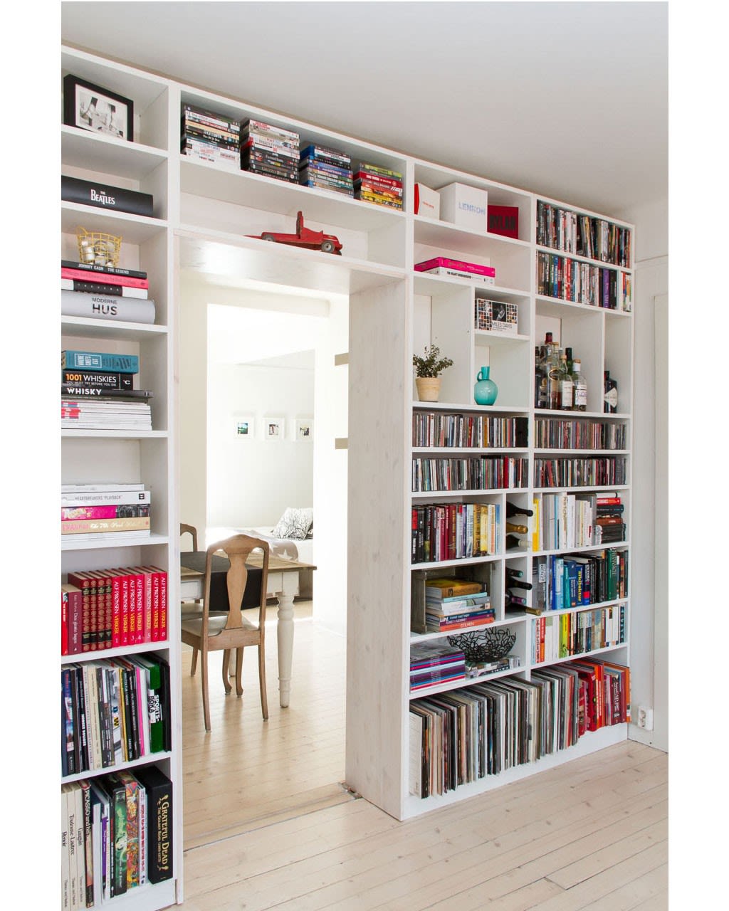 Hvit bokhylle rundt døråpning med fargerike bøker, plater, DVD, rød lekebil og turkis vase.