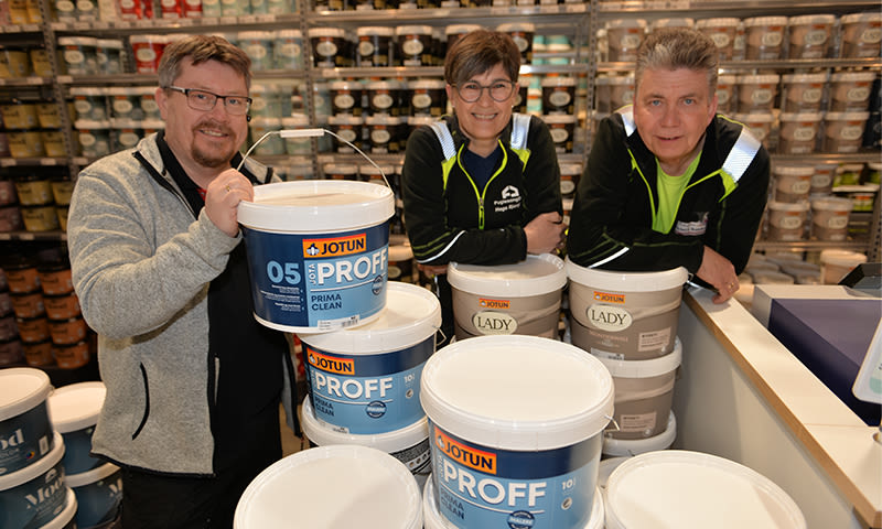 Tre ansatte bak disk med stabler av blå-hvite Jotun Proff- og Lady-maling i maltbutikk