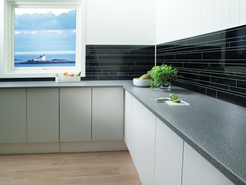 Lyst kjøkken med grå benkeplate, svart flisvegg, urter, lime og utsikt til sjø og fyr.