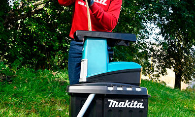 Person i rødt betjener en turkis Makita-batterilader på svart Makita-kasse i gress.