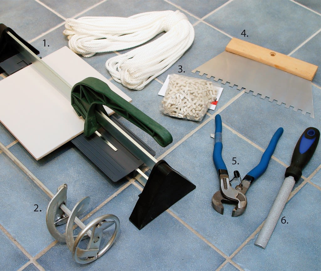 Flisleggerverktøy på blå gulvfliser: kutter, blandevisp, fliskryss, tannsparkel, flistang, fil