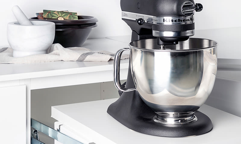 Svart KitchenAid-kjøkkenmaskin med rustfri stålbolle på hvit benkeplate ved morter.