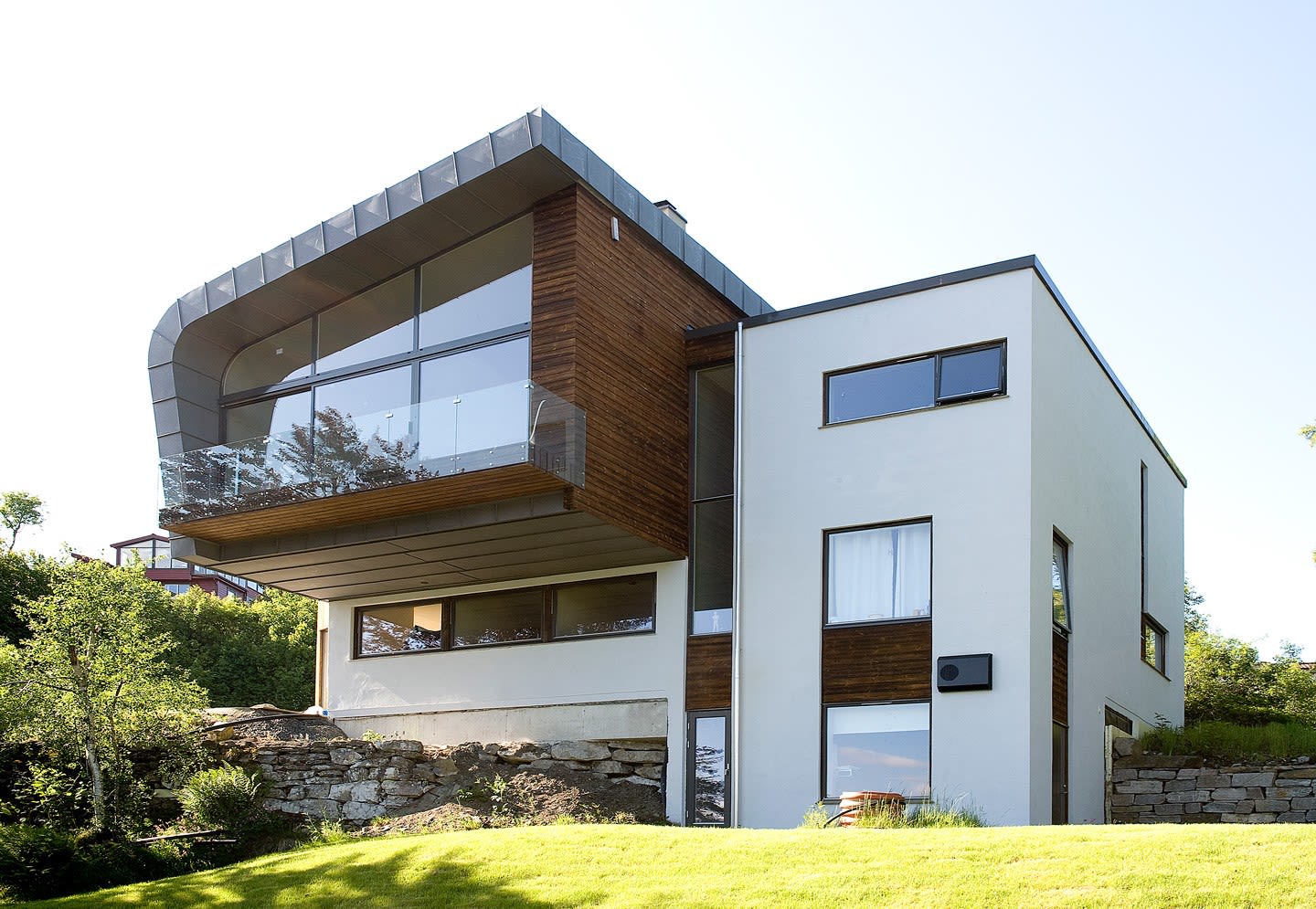 Moderne hvitt hus med trekledning, store vinduer, glassbalkong og grønt plen.