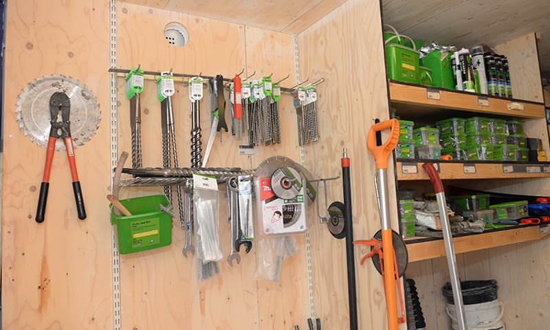 Trevegg i jernvarebutikk med rød boltesaks, sagblad, bor og grønne oppbevaringsbokser.