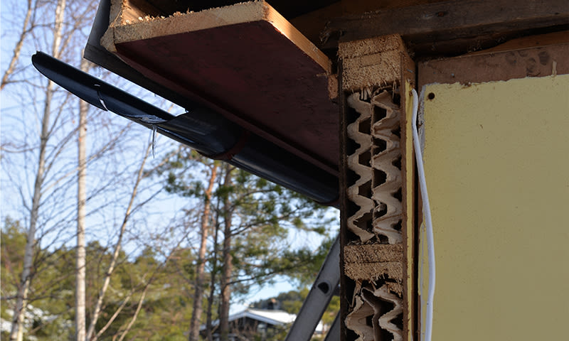 Nærbilde av huskrok med gul panel, eksponert murstein og svart takrenne mot blå himmel.