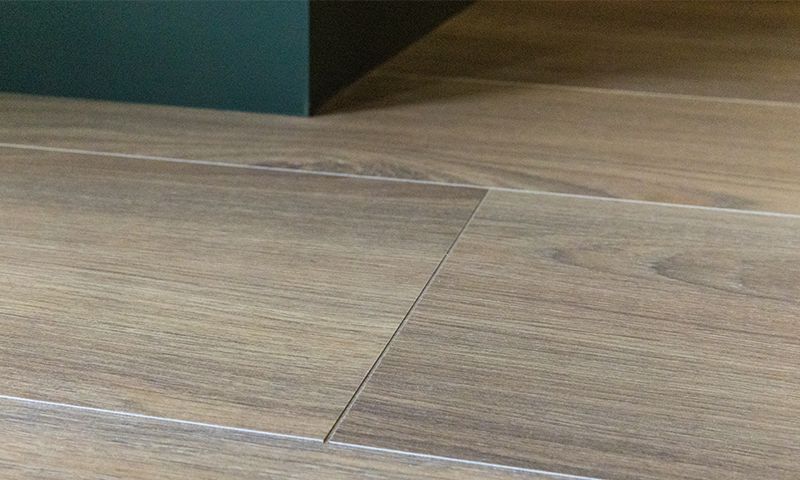 Lyst brunt tregulv med synlige skjøter mot en mørkegrønn sokkel