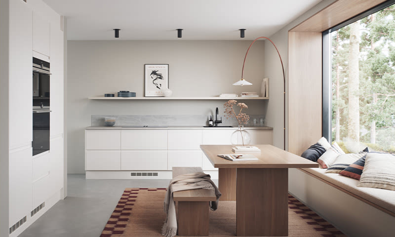 Lyst, minimalistisk kjøkken med hvite skap, trebord og benk, vindusplass med puter, rød buegulvlampe