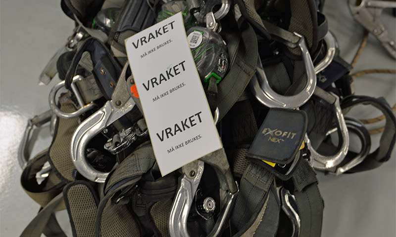 Grå fallsikringsseler med blanke metallkroker og hvite "VRAKET"-merkelapper.