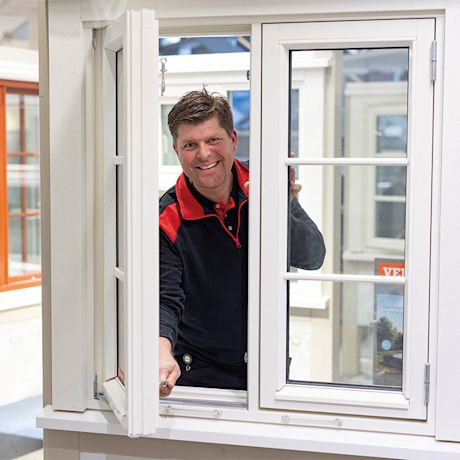 Montør i svart- og rød arbeidsjakke justerer hvit vindusramme i utstillingslokale