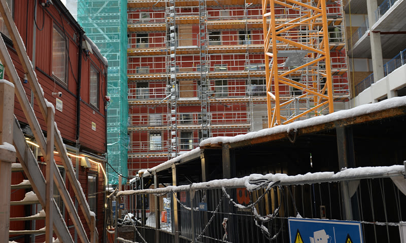 Vinterlig byggeplass med rød brakke, gul kran, stillas og snødekte containere