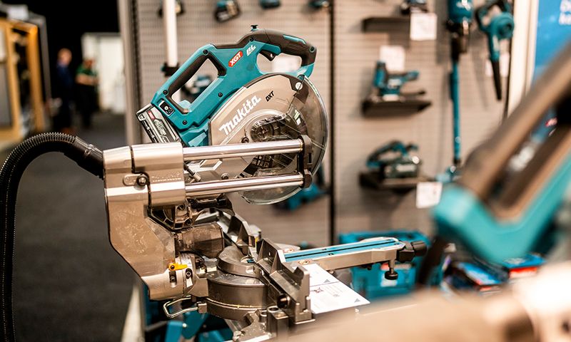 Turkis-sølv Makita kapp- og gjæringssag på messe, andre verktøy i bakgrunnen.