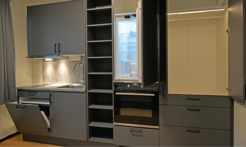 Moderne grå kjøkkenenhet med vask, åpen oppvaskmaskin, hyller, kjøleskap og skap