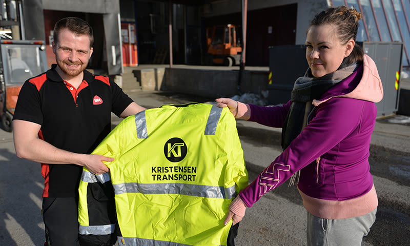 To personer holder neongul vernejakke med reflekstriper og KT-logo i industrimiljø.