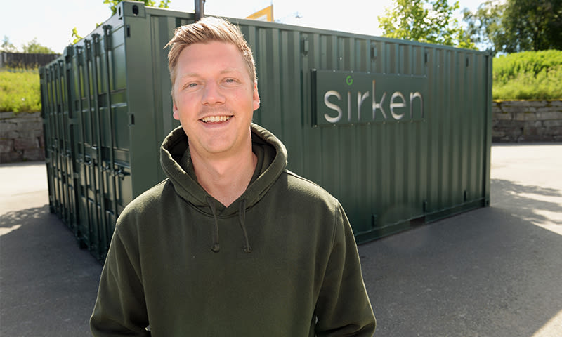 Person i olivengrønn hettegenser foran en mørkegrønn container merket "sirken"