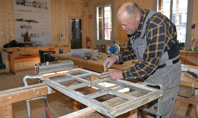 Tømrer i rutet skjorte skraper vindusramme med meisel i lyst treverksted