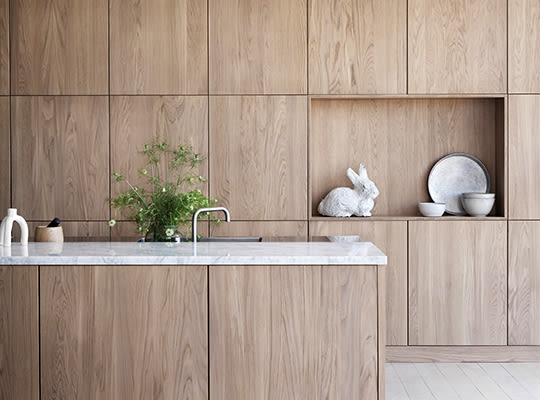 Moderne kjøkken med lyse tremøbler, marmorbenkeplate, grønn plante og hvit kaninskulptur.