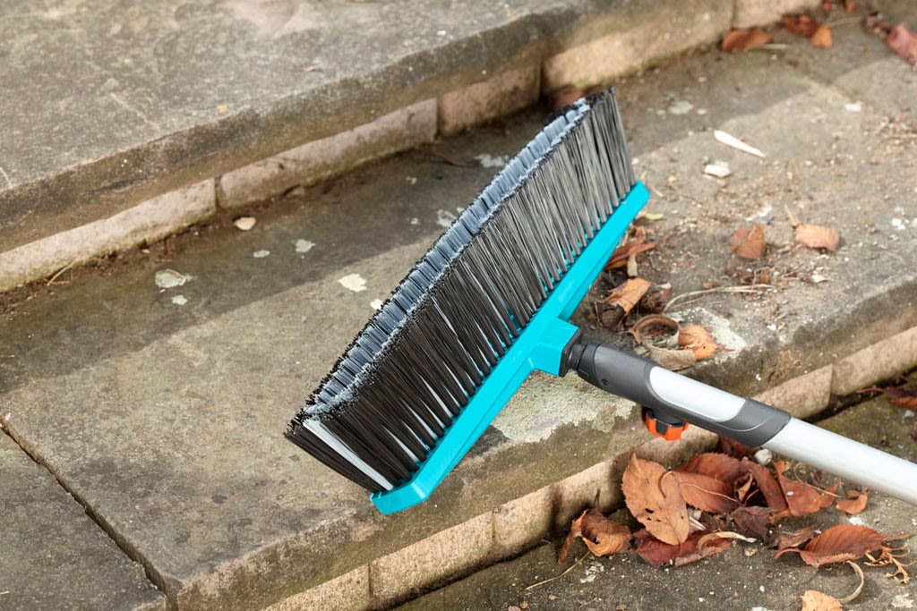 En turkis kost med grå bust feier brune høstblader fra grå steintrapp.