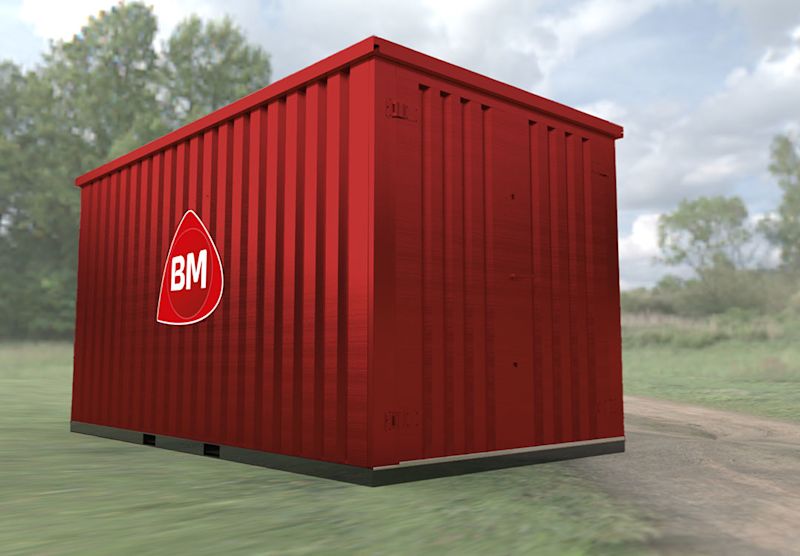 Rød metallcontainer med hvit BM-logo stående på gressbakke ved grusvei, trær i bakgrunnen.