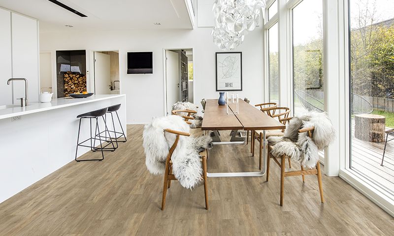 Lyst, moderne kjøkkenøy med svarte barstoler og trebord med skinnfeller foran store vinduer.