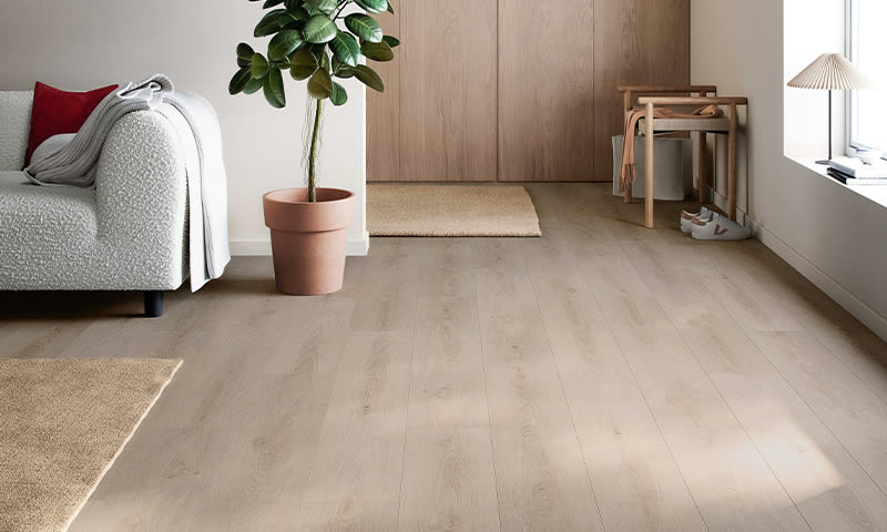 Lyst stuehjørne med lyst tregulv, hvit sofa med rød pute, potteplante og trebenk