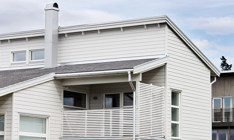 Moderne hvitt trehus med skråtak, pipe og hvit spileveranda.