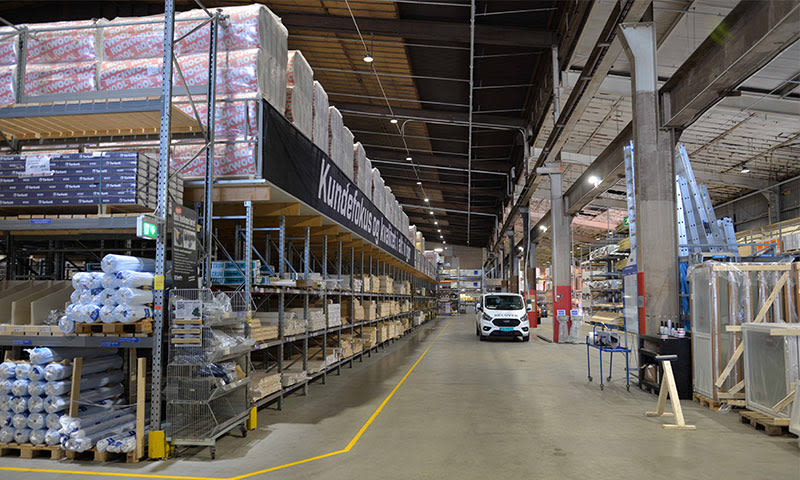 Stort byggvarelager med høye hyller fulle av isolasjon og en hvit varebil i midtgangen.