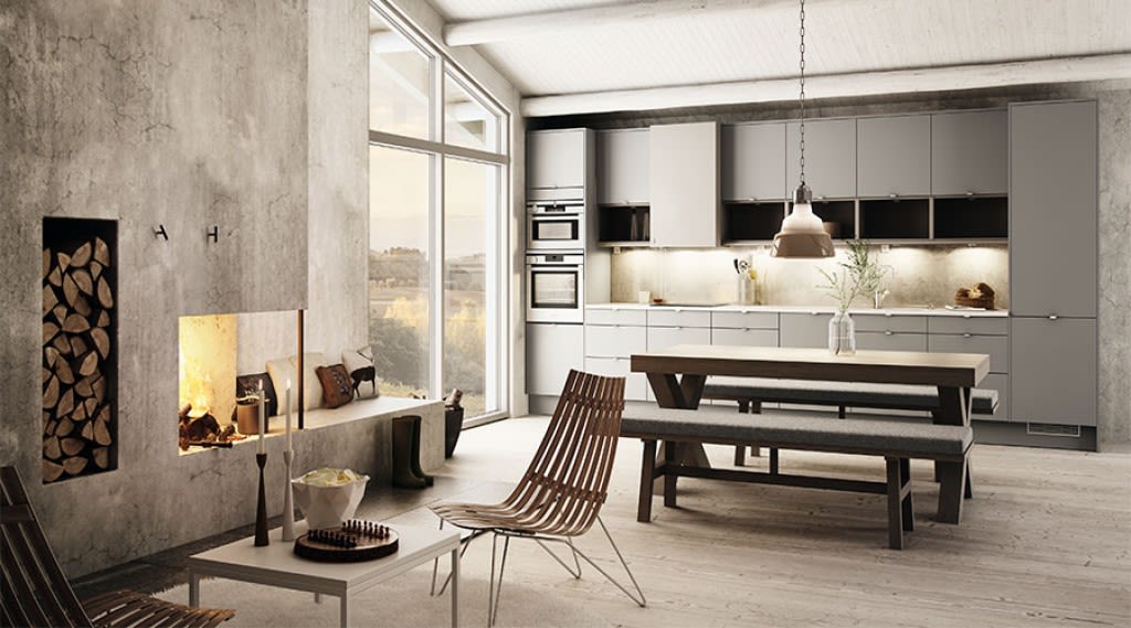 Lyst moderne kjøkken-stue med grå innredning, langt trebord med benker og peis.