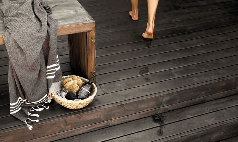 Mørk trekledning med grått håndkle, kurv med spa-produkter, våte fotavtrykk og barbent person