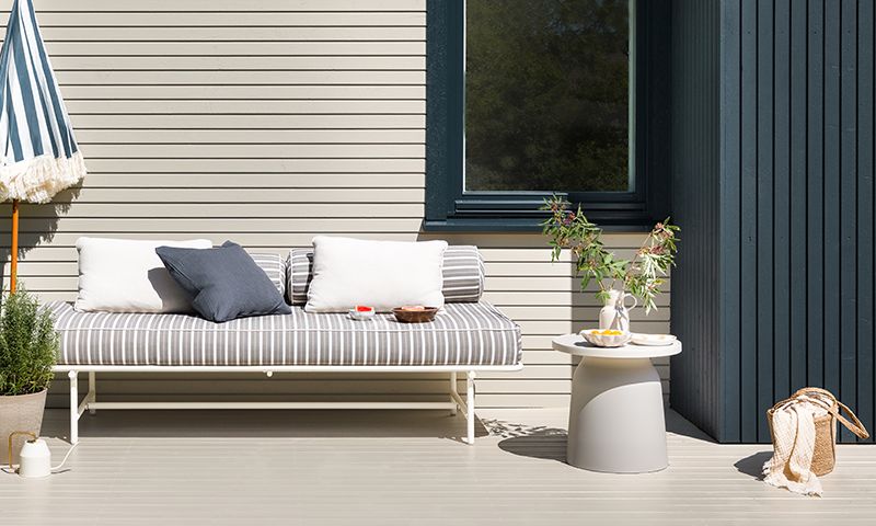 Solfylt uteområde med grå-hvitt stripet sjeselong, puter, sidebord med grønn kvist