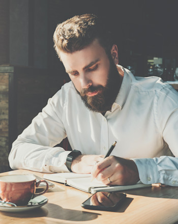 A bearded male writer taking notes for his novel.