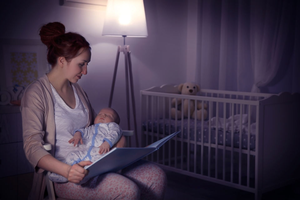 Madre leyéndole a su recién nacido en una habitación con poca luz