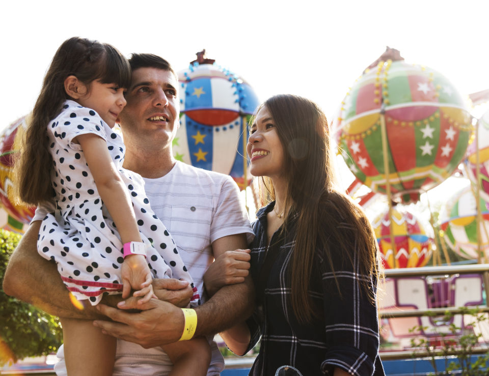 Father holding daughter at amusement park, mother smiling